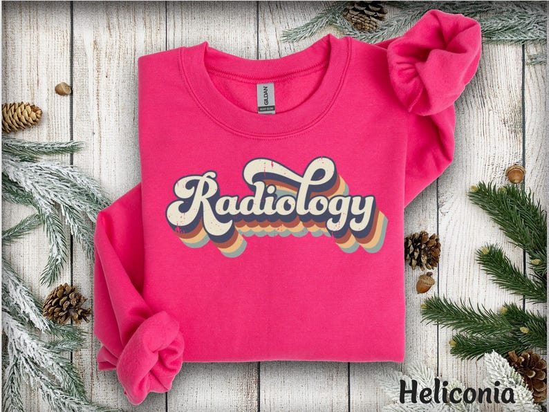 May include: A bright pink sweatshirt with the word "Radiology" in a retro font. The text is layered with a rainbow of colors, including blue, orange, and brown. The sweatshirt is a crew neck style.