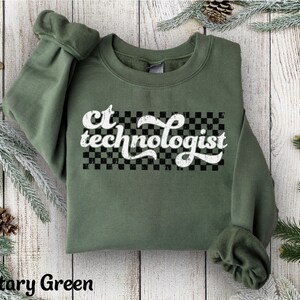 May include: Military green sweatshirt with the text "ct technologist" in a white, retro font over a black and white checkered rectangle. The sweatshirt has long sleeves and a crew neck.