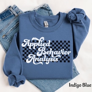 May include: Indigo blue sweatshirt with a white graphic that says "Applied Behavior Analysis" with a black and white checkered background.