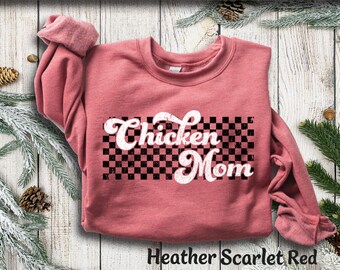 May include: Heather Scarlet Red sweatshirt with the text "Chicken Mom" in a white, retro font over a black and white checkered design. The long-sleeved top is a muted red color.
