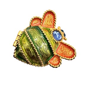 May include: A gold-tone brooch in the shape of a bee with green and orange enamel details. The bee has a blue gem for an eye.