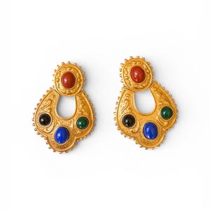 Peut inclure: Une paire de boucles d'oreilles dorées au design orné. Chaque boucle d'oreille comporte une pierre précieuse rouge, noire, bleue et verte. Les boucles d'oreilles ont un dessus décoratif en forme d'éclat de soleil et une forme de goutte.