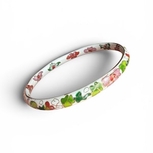 May include: A white bangle bracelet featuring a delicate cloisonné design with hand-painted floral motifs in shades of pink, red, and green, outlined with thin gold-toned metal wire, creating a continuous pattern around the entire circular band.