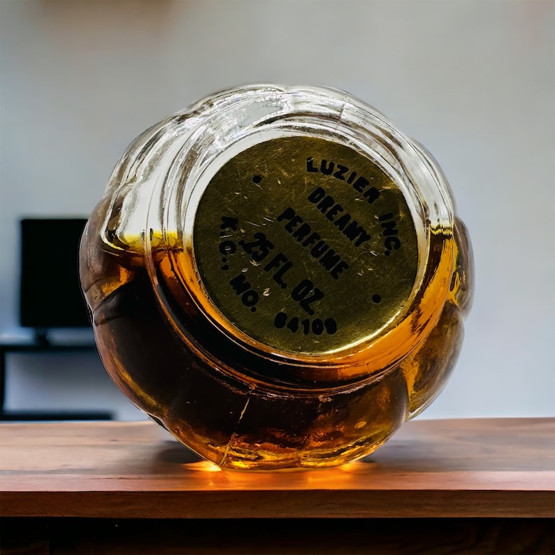 May include: A clear glass bottle with a gold-colored cap. The cap has the text "Luzier Inc. Dreamy Perfume 2.5 Fl. Oz. Reg. No. 84108" printed on it.
