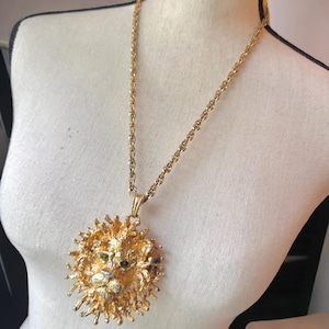 May include: Gold-tone lion pendant necklace. The pendant features a detailed lion's head with green and clear accents. The necklace has a long chain and is displayed on a mannequin.