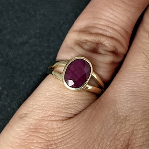 May include: A gold ring with a deep red oval gemstone set in a simple, elegant design.