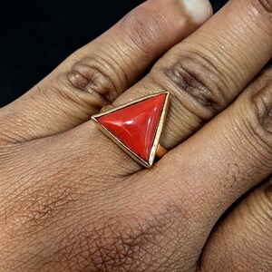 Puede incluir: Un anillo de oro con una piedra preciosa de coral rojo triangular.