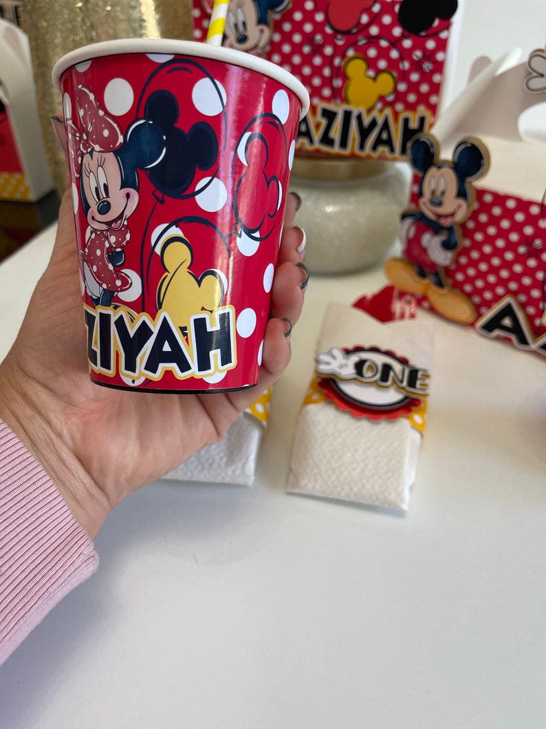 May include: Red and white paper cup with a Mickey Mouse and Minnie Mouse design. The cup has the name "Aziyah" printed on it.
