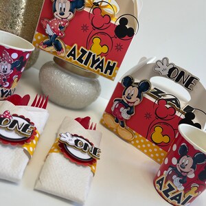 May include: Red and yellow Mickey Mouse and Minnie Mouse themed party supplies.  The set includes two red and yellow cups with Mickey Mouse and Minnie Mouse images, two red and yellow napkins with Mickey Mouse and Minnie Mouse images, two red and yellow boxes with Mickey Mouse and Minnie Mouse images, and two red and yellow forks with Mickey Mouse and Minnie Mouse images. The boxes have the words "One" and "Aziyah" on them.