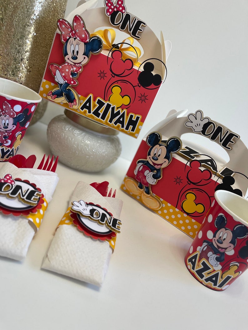 May include: Red and yellow Mickey Mouse and Minnie Mouse themed party supplies.  The set includes two red and yellow cups with Mickey Mouse and Minnie Mouse images, two red and yellow napkins with Mickey Mouse and Minnie Mouse images, two red and yellow boxes with Mickey Mouse and Minnie Mouse images, and two red and yellow forks with Mickey Mouse and Minnie Mouse images. The boxes have the words "One" and "Aziyah" on them.