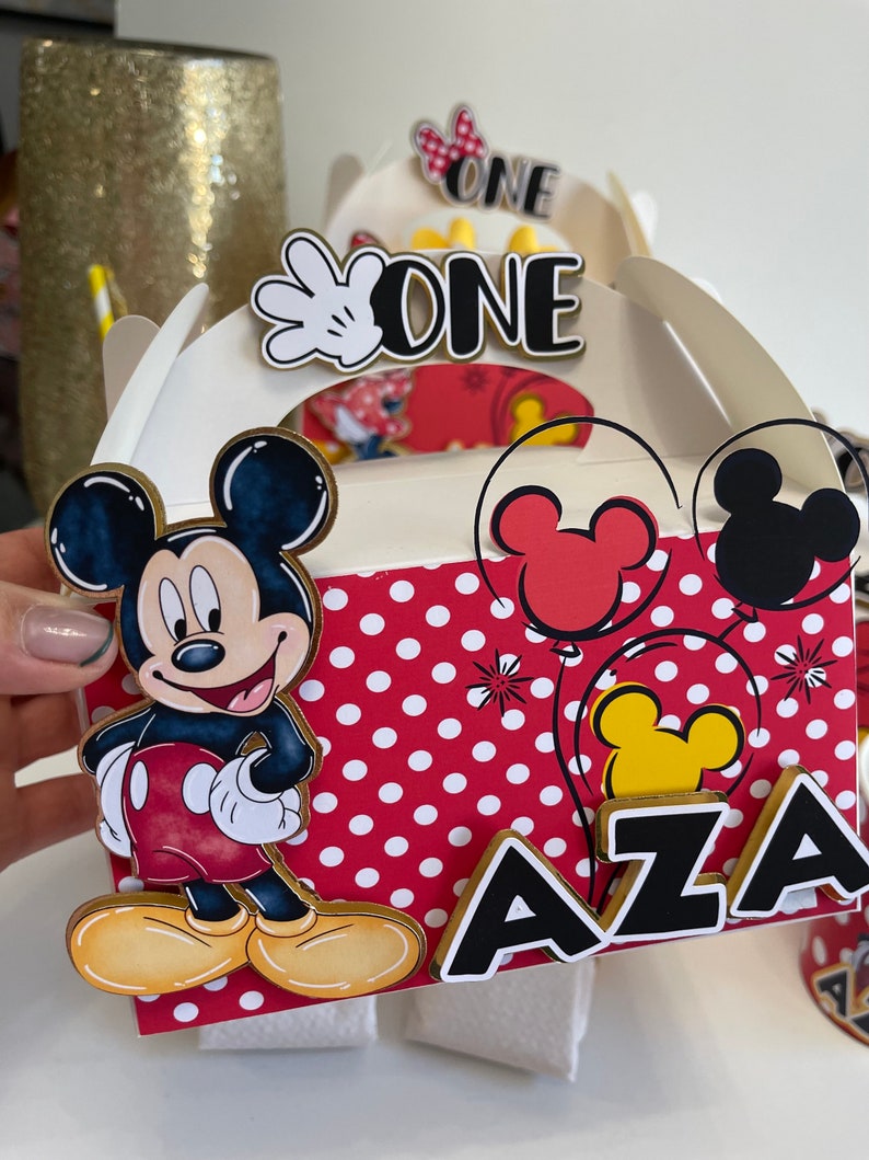 May include: A red and white polka dot box with a Mickey Mouse character on the front. The box has a gold trim and says "AZA" and "ONE" on it.