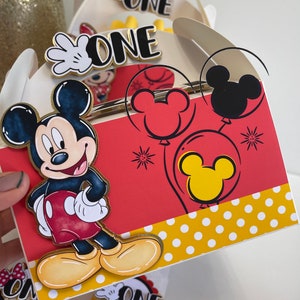 May include: Red and white Mickey Mouse themed party favor boxes with a Mickey Mouse character on the front and the word "ONE" on the top. The boxes have yellow polka dots on the bottom and red and yellow Mickey Mouse balloons on the side.