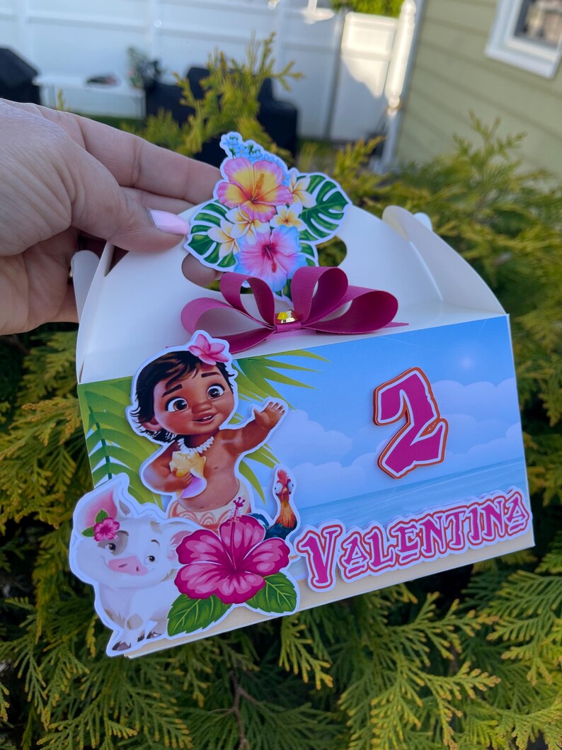 May include: A white party favor box featuring a cartoon illustration of a young girl, a pig, and a rooster. The box is decorated with tropical flowers, the number 2, and the name "Valentina". A pink bow and flower accents the top.