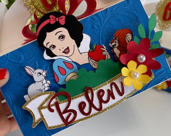 May include: A blue box with a Snow White theme, featuring a cartoon image of Snow White, a red apple, and a squirrel. The box is decorated with a red bow, a gold number 6, and the name "Belen" in red glitter.