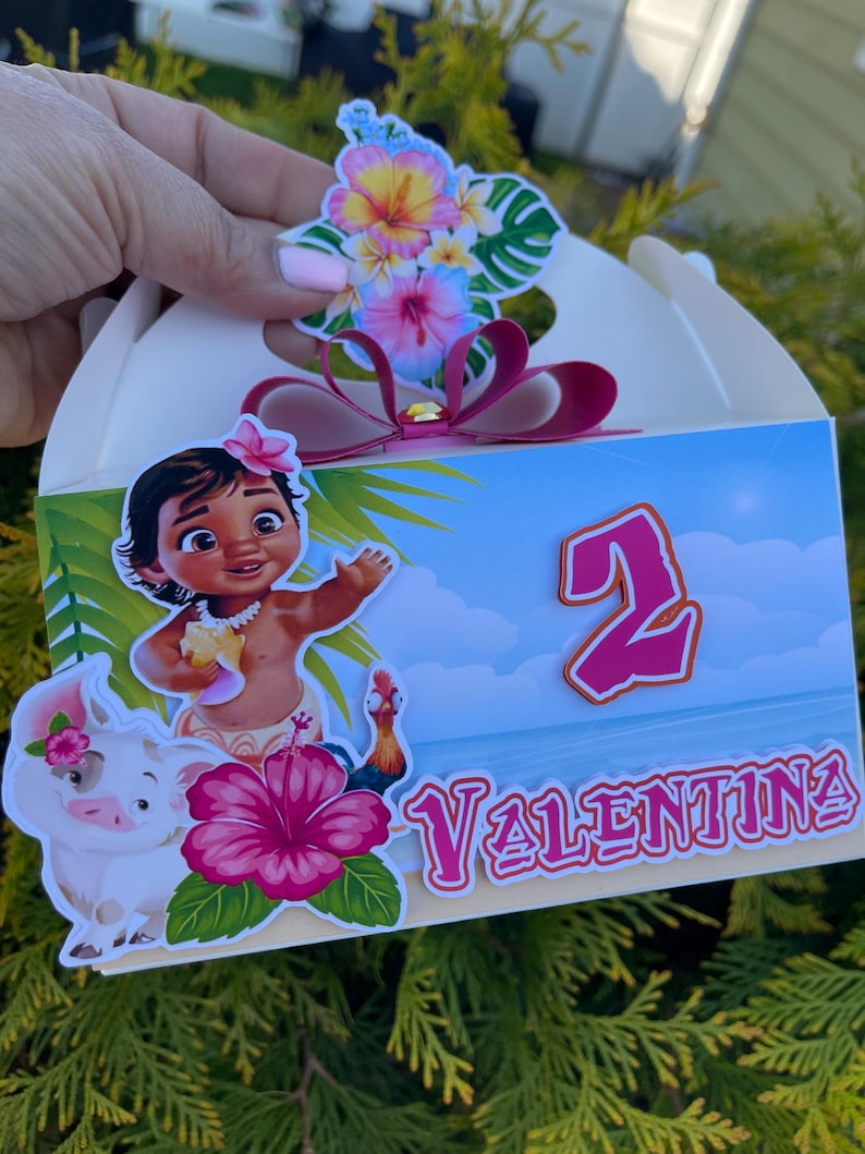 May include: A white party favor box decorated with a tropical theme. The box features a cartoon image of a girl, a pig, and a rooster. The box is decorated with the name "Valentina" and the number "2".