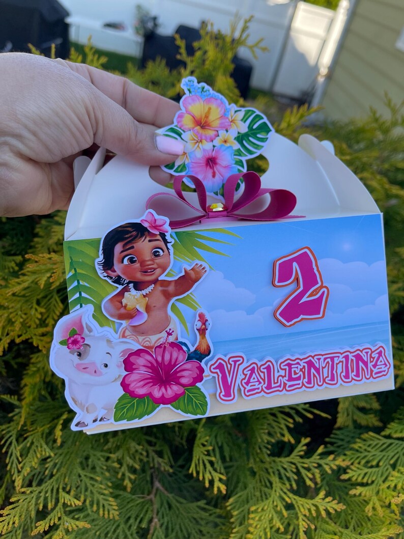 May include: A white party favor box with a tropical theme. The box features a cartoon illustration of a girl, a pig, and a rooster. The box is decorated with a pink hibiscus flower, the number 2, and the name "Valentina".