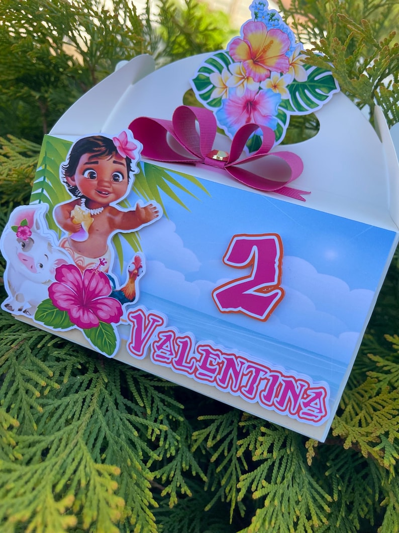 May include: A white gift box decorated with a cartoon image of a girl, a pig, and tropical flowers. The box features the number 2 and the name "Valentina" in pink. A pink bow and floral arrangement adorn the top.
