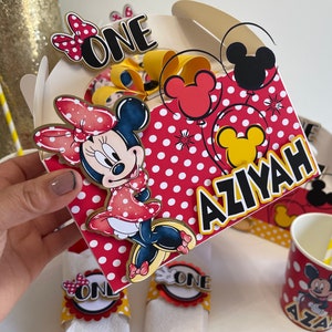 May include: Red and white polka dot party favor boxes with a Mickey Mouse and Minnie Mouse theme. The boxes are decorated with red and yellow balloons, a Minnie Mouse character, and the text "ONE" and "AZIYAH".