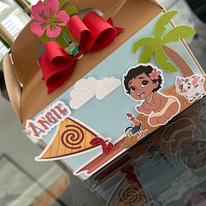 May include: A brown cardboard party favor box decorated with a red bow, a green palm tree, a white cloud, a cartoon image of a baby Moana, a rooster, and a pig. The box has the name "Angie" written on it.