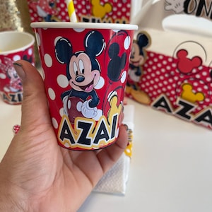 May include: Red and white paper cup with a Mickey Mouse design. The cup has white polka dots and the name "AZAI" printed on the bottom.