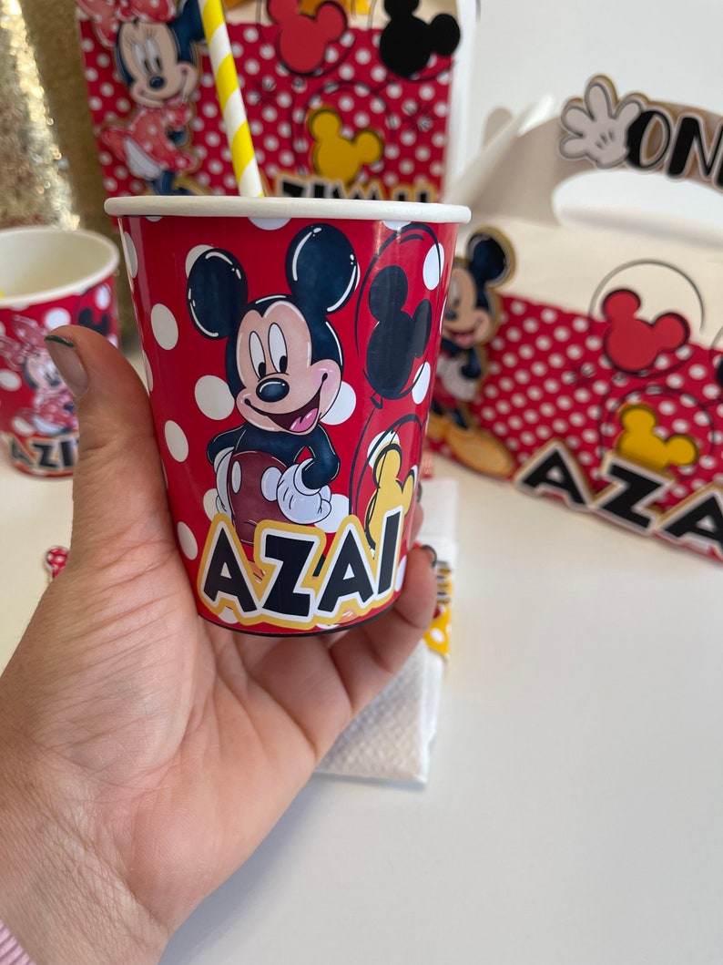 May include: Red and white paper cup with a Mickey Mouse design. The cup has white polka dots and the name "AZAI" printed on the bottom.
