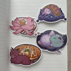 May include: Four colorful stickers featuring cartoon animals enjoying different foods. A pink fox with a bushy tail is in a bowl of ramen, a purple and blue creature is in a taco, a purple and blue creature is on a pillow, and a purple creature is in a bowl of rice with a fried egg on top.