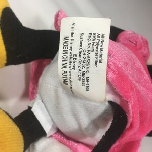 May include: A pink and yellow plush toy with black eyes and a white belly. The toy has a tag that reads "All New Material All Polyester Fiber EVA Foam Reg. No. PA-6525(HK), MA-1108 OH-21432, ME-3955 Surface Clean Only, Air Dry Visit the Disney website at www.disney.com &copy;Disney MADE IN CHINA, PUTIAN".