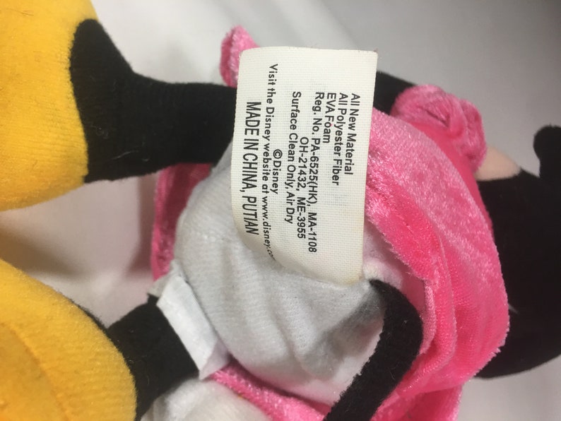 May include: A pink and yellow plush toy with black eyes and a white belly. The toy has a tag that reads "All New Material All Polyester Fiber EVA Foam Reg. No. PA-6525(HK), MA-1108 OH-21432, ME-3955 Surface Clean Only, Air Dry Visit the Disney website at www.disney.com &copy;Disney MADE IN CHINA, PUTIAN".