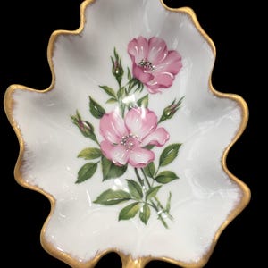May include: A white porcelain leaf-shaped dish with a gold rim and a painted design of pink roses with green leaves.
