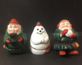 Puede incluir: Tres figuras de cerámica de personas que llevan túnicas verdes y sombreros rojos. La figura del medio es un muñeco de nieve con un pájaro rojo en la cabeza. Las figuras miden aproximadamente 13 cm de alto.