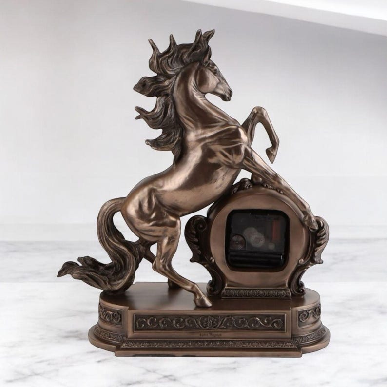 May include: Bronze-colored horse clock with a rearing horse design. The clock features a detailed sculpture of a horse with flowing mane and tail, leaning on a decorative clock face. The base has an ornate, scrolled design.