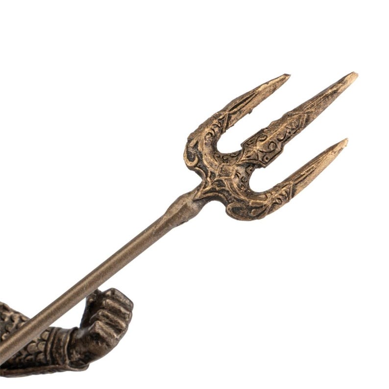 May include: A bronze trident with ornate detailing on the three prongs and the central section. The handle is a simple, slender rod. The trident is held by a bronze arm with scale-like armor.