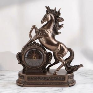 May include: Bronze-colored decorative clock featuring a rearing horse. The clock has an ornate, vintage design with a round clock face and Roman numerals. The horse statue is detailed and adds a touch of elegance to the home decor.