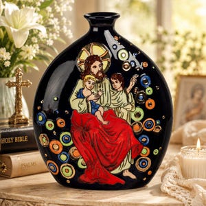 Könnte beinhalten: Eine schwarze Keramikvase mit einer handbemalten Illustration einer bärtigen Figur in rotem Gewand, die ein Kind hält, umgeben von einem dekorativen Muster aus kleinen, leuchtend bunten Kreisen und einem goldenen Heiligenschein hinter dem Kopf.