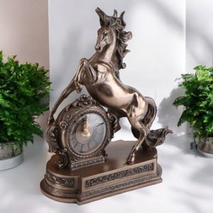 May include: Bronze-colored decorative clock featuring a rearing horse sculpture. The clock has an ornate, circular face with Roman numerals and a detailed base. The horse is the focal point, adding a touch of elegance to the home decor.