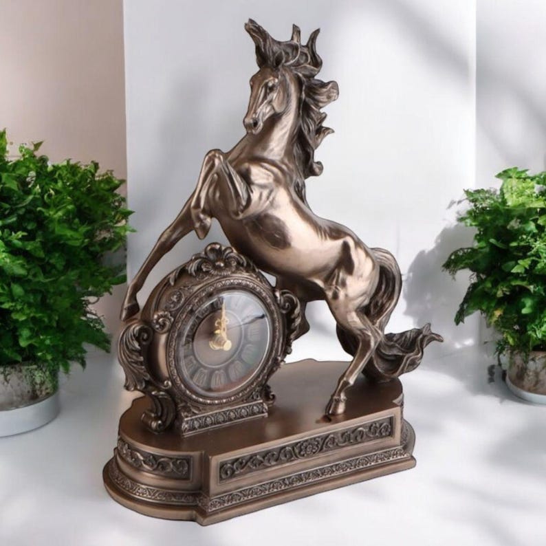 May include: Bronze-colored decorative clock featuring a rearing horse sculpture. The clock has an ornate, circular face with Roman numerals and a detailed base. The horse is the focal point, adding a touch of elegance to the home decor.