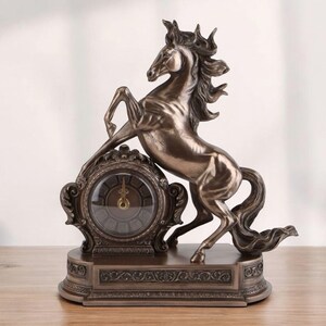 May include: Bronze-colored decorative clock featuring a rearing horse sculpture. The clock has an ornate, circular face with Roman numerals and a detailed base. A stylish home decor item.