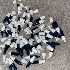 May include: A pile of blue and clear Christmas light bulbs with white plastic bases. The bulbs are arranged in a random pattern and are ready to be used for decorating a Christmas tree.