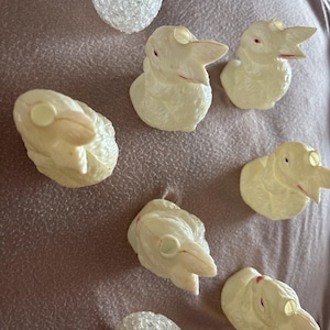 Peut inclure: Une collection d'ornements de canard en plastique blanc cassé vintage et deux ornements d'ampoule clairs et texturés. Les ornements de canard ont des becs ouverts et des accents rouges. Les articles sont disposés sur une surface mauve.