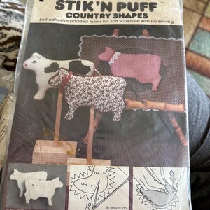 May include: A package of Banar Designs Stik 'N Puff Country Shapes. The package features self-adhesive padded forms for soft sculpture with no sewing. The shapes include a cow, sheep, and pig. The package also includes instructions and a cutting pattern.