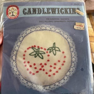 May include: A vintage "Candlewicking" kit in a plastic package. The kit features a white fabric circle with embroidered strawberries, red dots, and green leaves, surrounded by white lace. The package includes text about the contents.