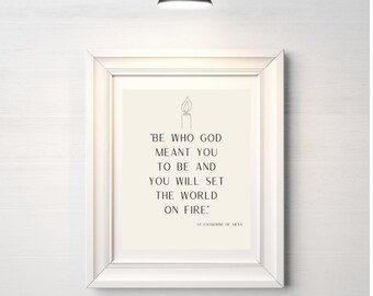 May include: A white framed print with a black and white quote that reads 'Be who God meant you to be and you will set the world on fire: St. Catherine of Siena'.