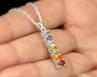 May include: Silver necklace with a pendant featuring seven colorful gemstones in a vertical row. The gemstones are purple, blue, green, yellow, orange, and red.