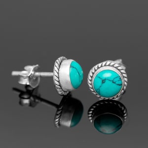 May include: A pair of silver stud earrings with turquoise stones. The earrings have a simple design with a round stone set in a silver bezel.