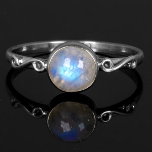 May include: A silver ring with a delicate, swirling design and a round, iridescent moonstone.