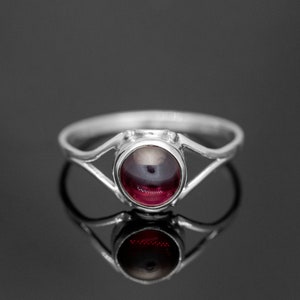 Peut inclure: Une bague en argent avec une pierre précieuse rouge foncé sertie dans un sertissage clos. La bague a un design délicat et ajouré.