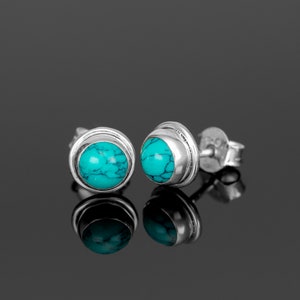 Op de afbeelding: Een paar zilveren oorbelletjes met turquoise stenen. De oorbelletjes hebben een simpel ontwerp met een ronde steen die in een zilveren zetting zit.