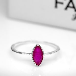 May include: A silver ring featuring a marquise-shaped ruby gemstone. The ring has a textured band and a delicate setting for the stone.