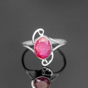 May include: A silver ring with a delicate, swirling design features a vibrant pink oval-shaped gemstone.