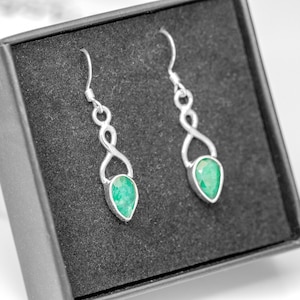 May include: A pair of silver earrings with green gemstone drops. The earrings feature a delicate, intertwined design.